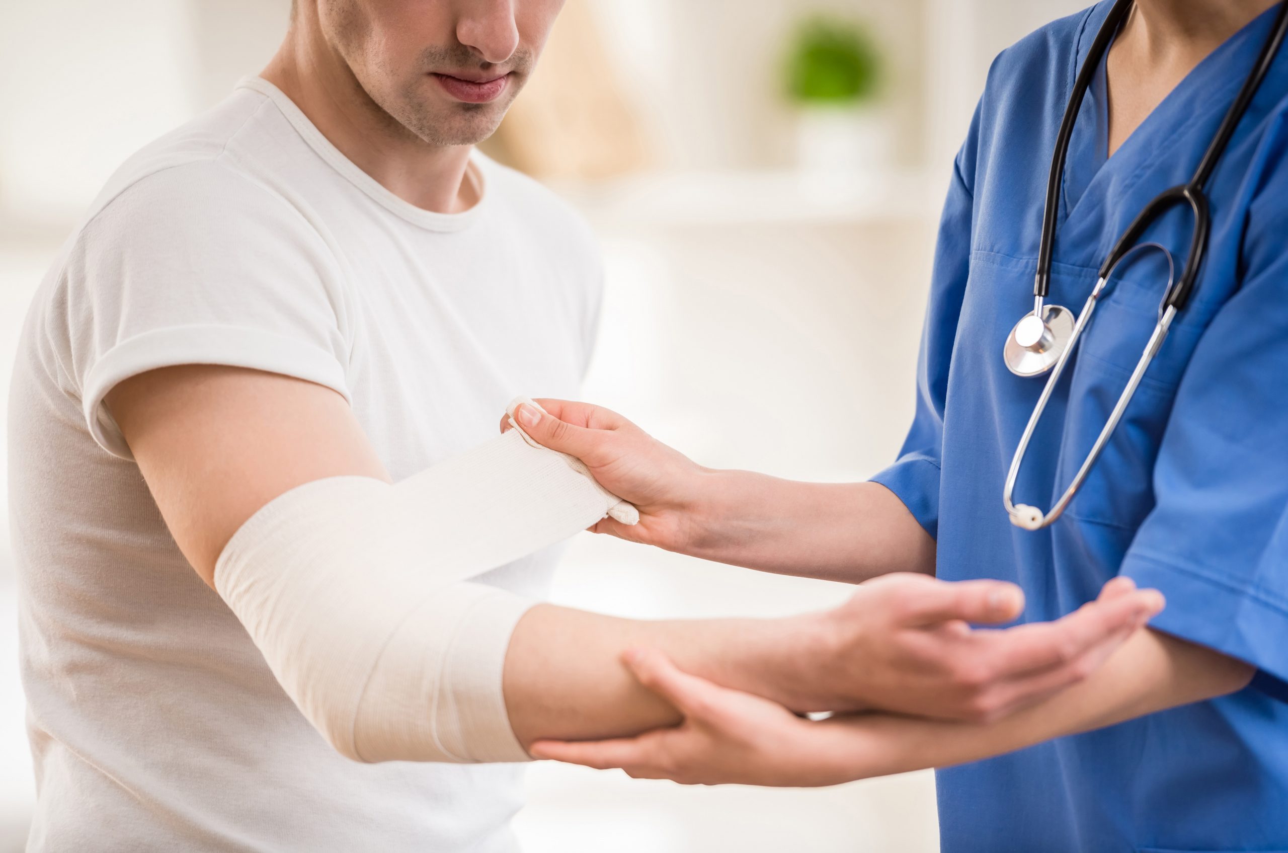 Close-up of female doctor with stethoscope  bandaging hand of male patient.